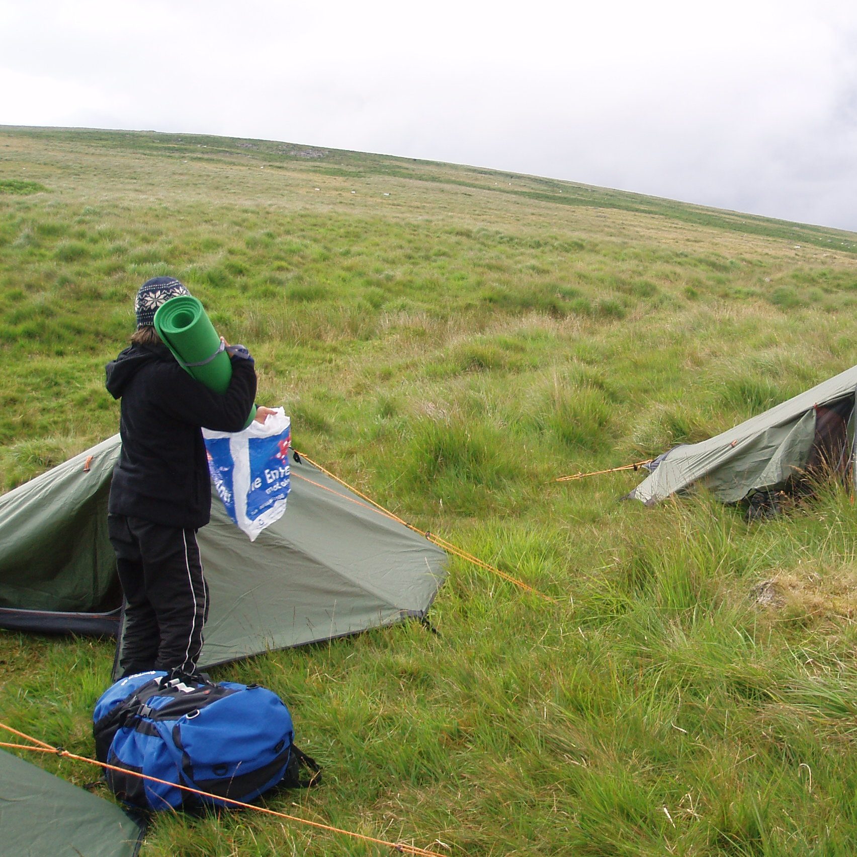 A child holding a roll mat next to a small tent